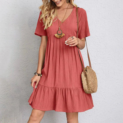 Red - A woman wearing a camel-colored, short-sleeved crinkle gauze mini dress with a V-neckline, empire waist, and tiered ruffled hem, styled with a straw shoulder bag.