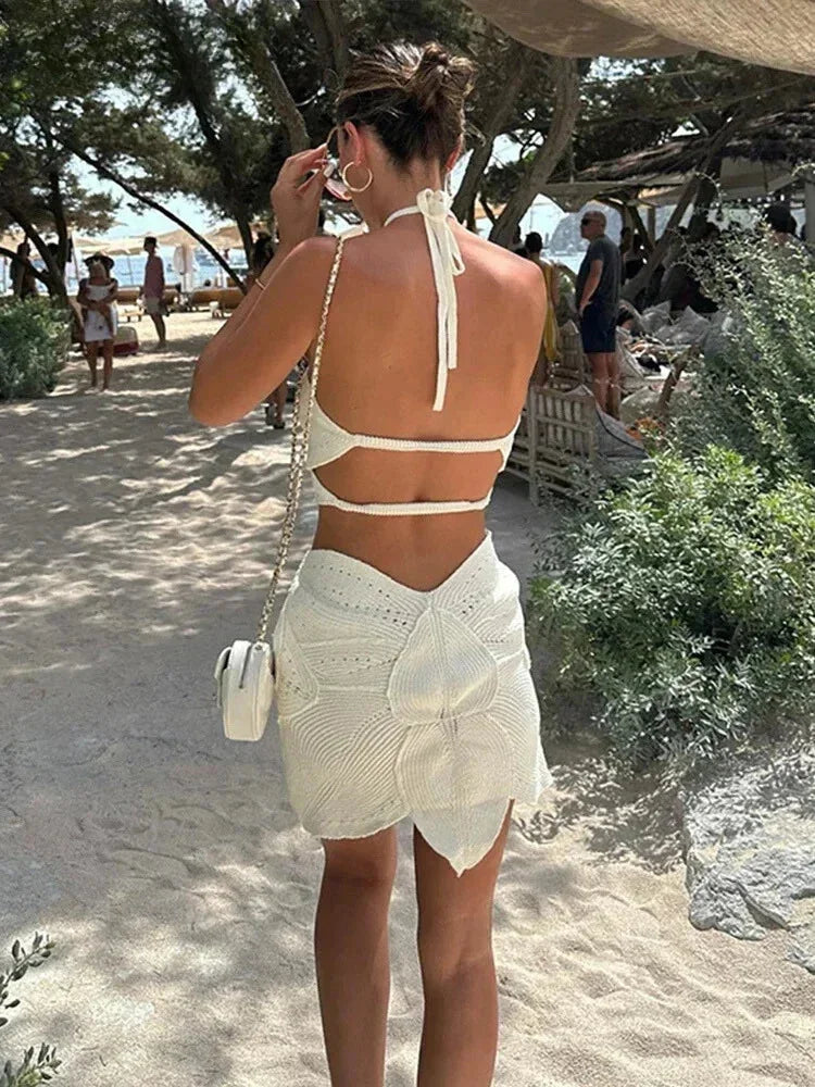 White - White crochet halter mini dress featuring large botanical cutouts, an asymmetrical hem, and an open waist design.