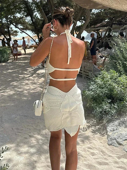 White - White crochet halter mini dress featuring large botanical cutouts, an asymmetrical hem, and an open waist design.