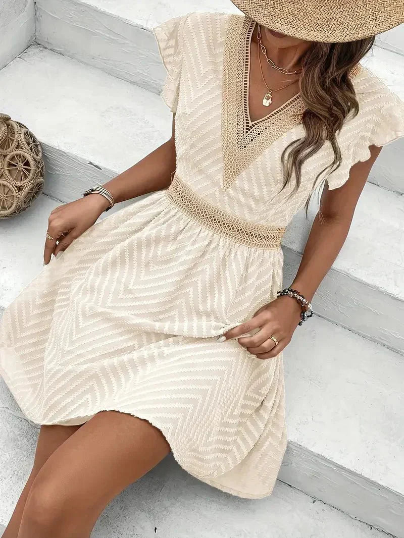 White - Woman wearing a short A-line dress with short flutter sleeves, featuring a raised chevron texture and crochet trim at the deep V-neckline and waist