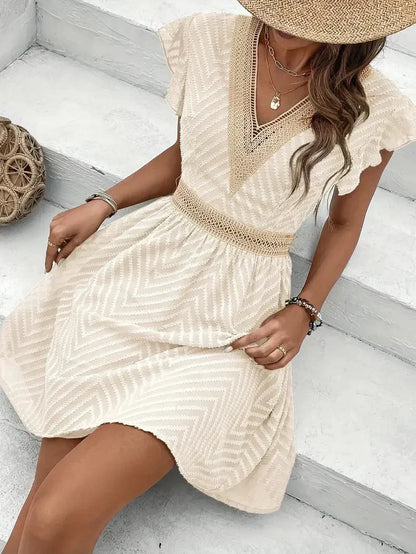 White - Woman wearing a short A-line dress with short flutter sleeves, featuring a raised chevron texture and crochet trim at the deep V-neckline and waist