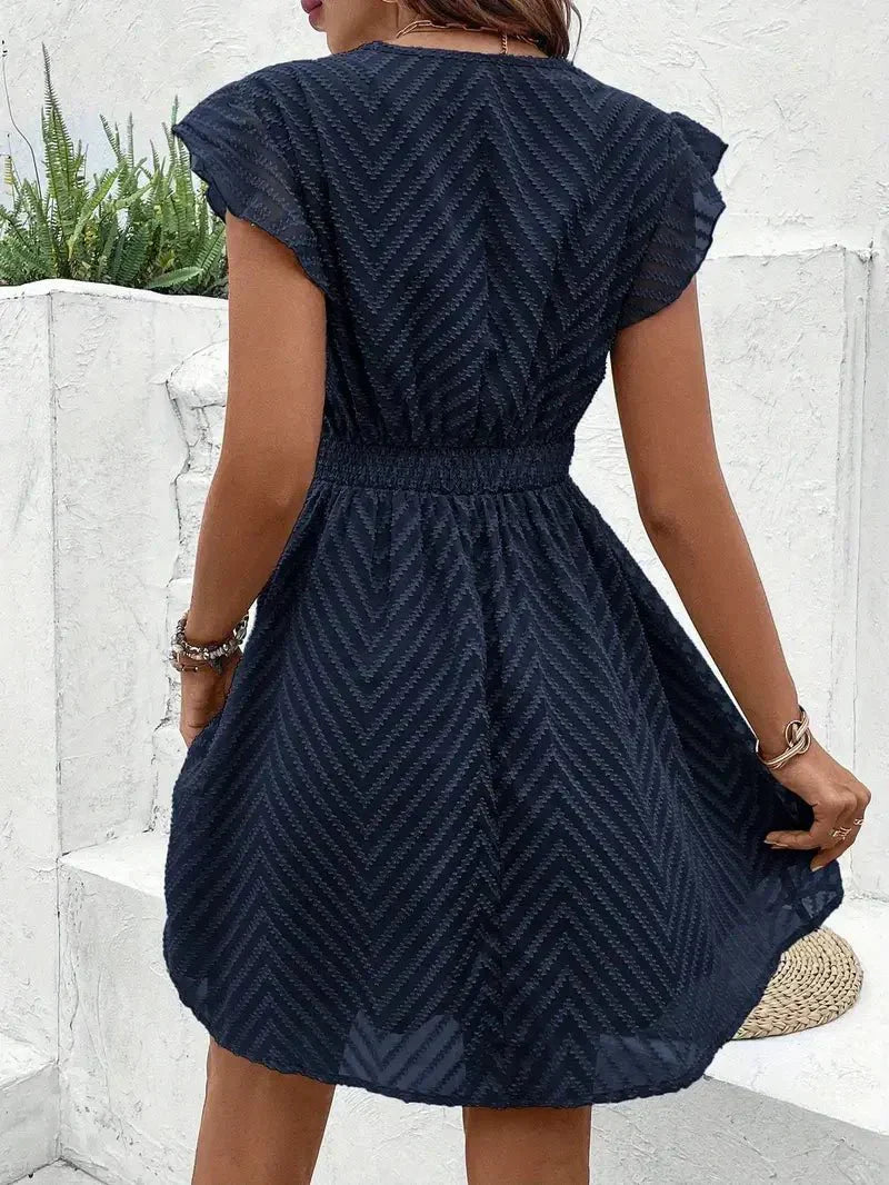 White - Woman wearing a short A-line dress with short flutter sleeves, featuring a raised chevron texture and crochet trim at the deep V-neckline and waist