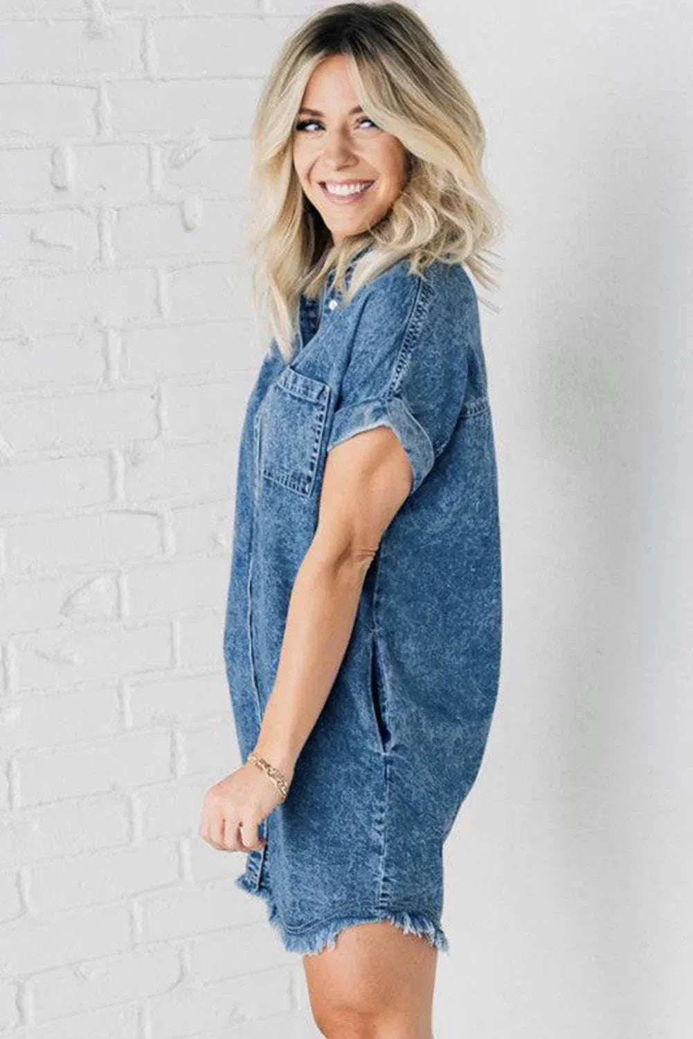 Blue - Woman wearing a relaxed fit mottled wash denim mini shirt dress with rolled short sleeves, a button-front closure, and a frayed raw hem.