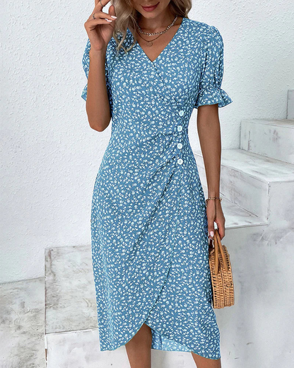 Blue - A woman wearing a blue and white ditsy floral midi dress featuring a V-neckline, ruched side detailing with white buttons, and short puff sleeves with ruffled cuffs.