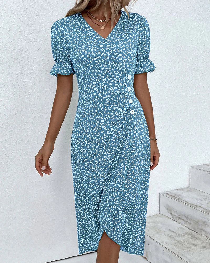 Blue - A woman wearing a blue and white ditsy floral midi dress featuring a V-neckline, ruched side detailing with white buttons, and short puff sleeves with ruffled cuffs.