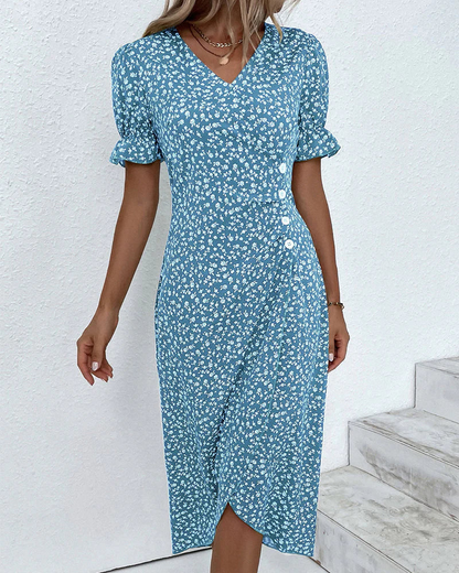 Blue - A woman wearing a blue and white ditsy floral midi dress featuring a V-neckline, ruched side detailing with white buttons, and short puff sleeves with ruffled cuffs.