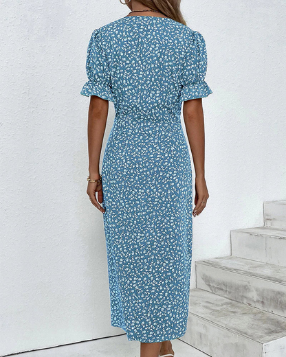 Blue - A woman wearing a blue and white ditsy floral midi dress featuring a V-neckline, ruched side detailing with white buttons, and short puff sleeves with ruffled cuffs.