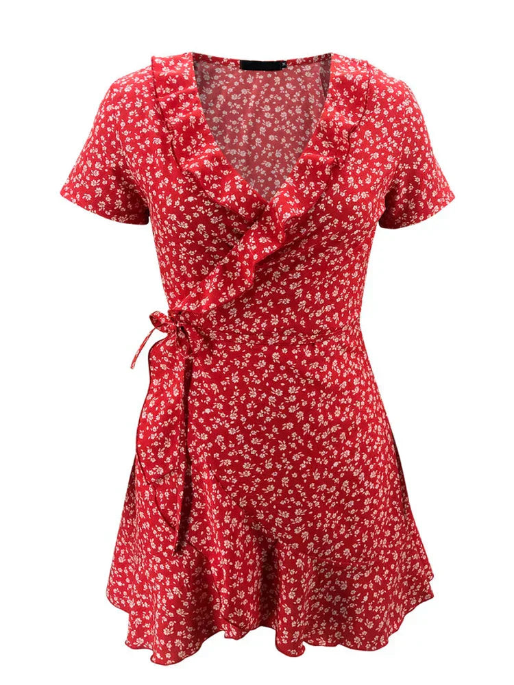 Red - A close-up of a person wearing a red wrap mini dress with a white ditsy floral print, featuring a ruffled V-neckline, short sleeves, and a tie-waist closure.
