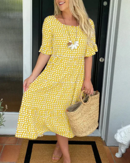 Yellow - A woman wearing a taupe and white dot print midi dress with a scoop neck, ruffled half sleeves, and a tiered skirt, holding a woven straw bag.