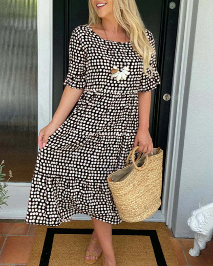 Black - A woman wearing a taupe and white dot print midi dress with a scoop neck, ruffled half sleeves, and a tiered skirt, holding a woven straw bag.