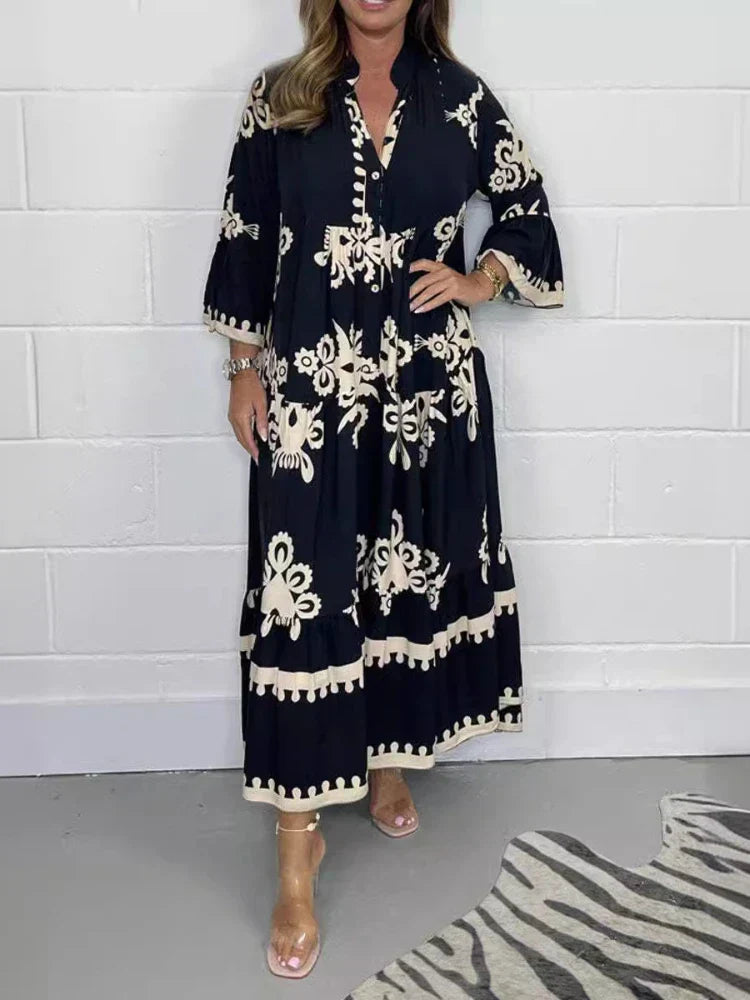 Black - A woman wearing a black maxi dress with cream-colored contrast embroidery, featuring three-quarter bell sleeves, a split V-neckline, and a tiered skirt with a scalloped hem.