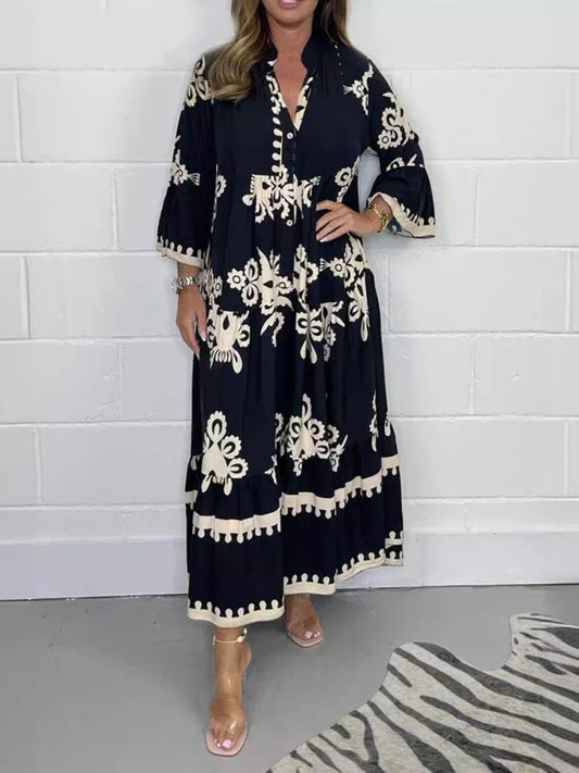Black - A woman wearing a black maxi dress with cream-colored contrast embroidery, featuring three-quarter bell sleeves, a split V-neckline, and a tiered skirt with a scalloped hem.