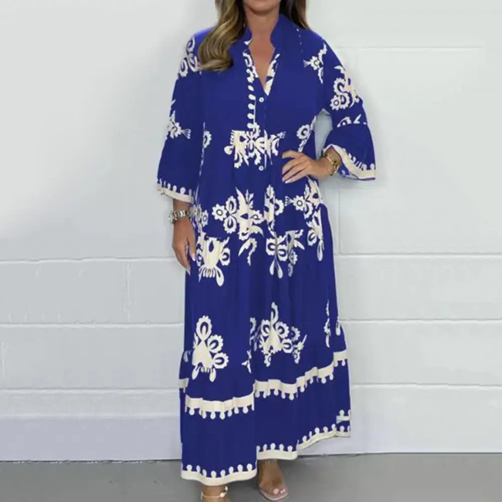 Blue - A woman wearing a black maxi dress with cream-colored contrast embroidery, featuring three-quarter bell sleeves, a split V-neckline, and a tiered skirt with a scalloped hem.