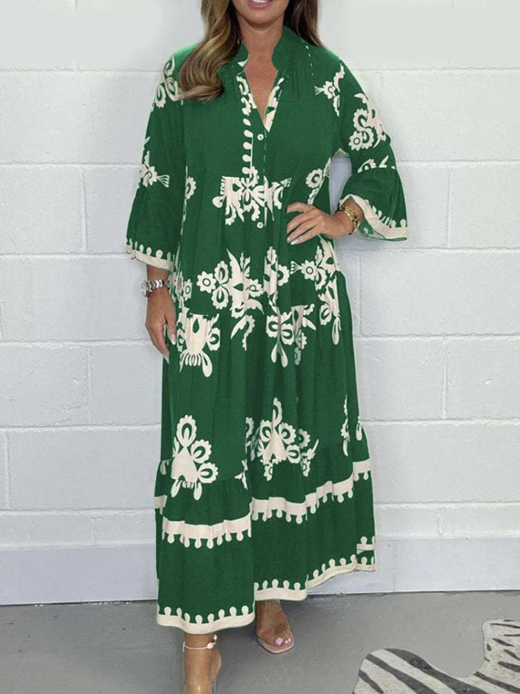 Green - A woman wearing a black maxi dress with cream-colored contrast embroidery, featuring three-quarter bell sleeves, a split V-neckline, and a tiered skirt with a scalloped hem.