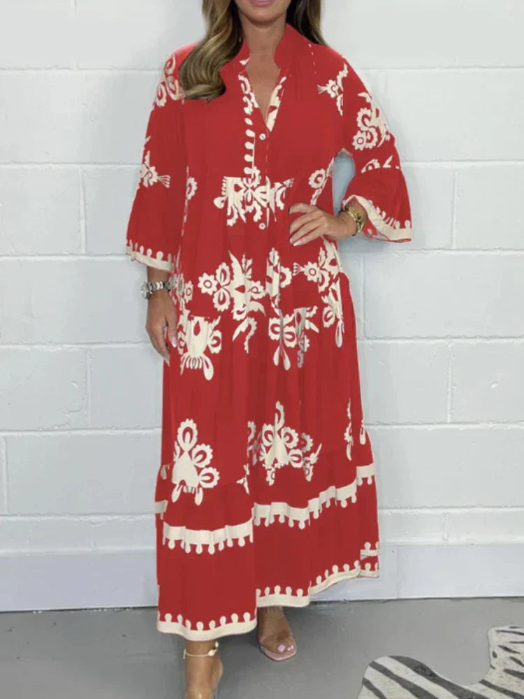 Red - A woman wearing a black maxi dress with cream-colored contrast embroidery, featuring three-quarter bell sleeves, a split V-neckline, and a tiered skirt with a scalloped hem.