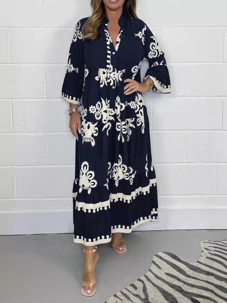 Navy Blue - A woman wearing a black maxi dress with cream-colored contrast embroidery, featuring three-quarter bell sleeves, a split V-neckline, and a tiered skirt with a scalloped hem.
