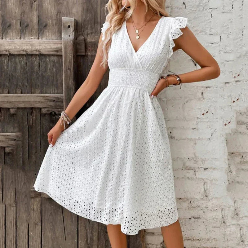 White - A woman wearing a white eyelet midi dress with flutter sleeves, a surplice V-neckline, and a wide smocked waistband, standing against a rustic wooden door.