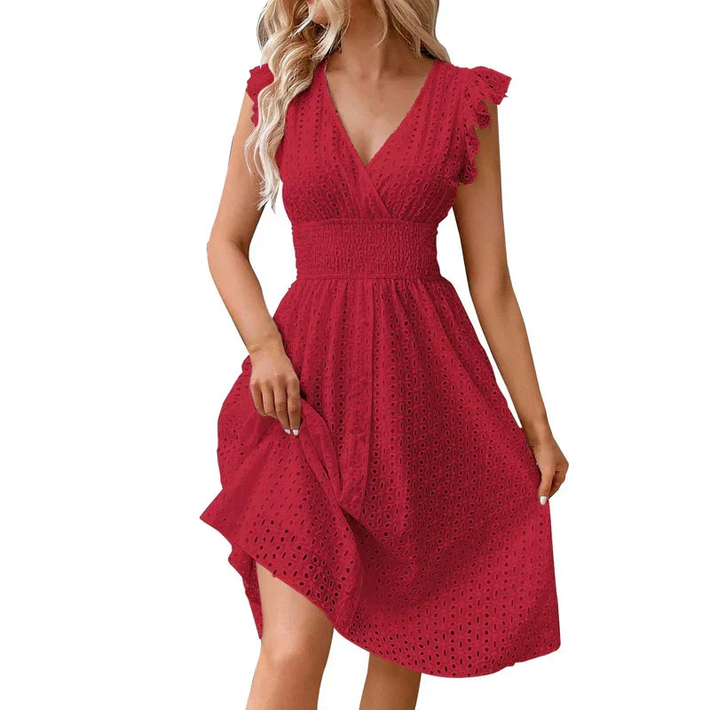 Red - A woman wearing a white eyelet midi dress with flutter sleeves, a surplice V-neckline, and a wide smocked waistband, standing against a rustic wooden door.