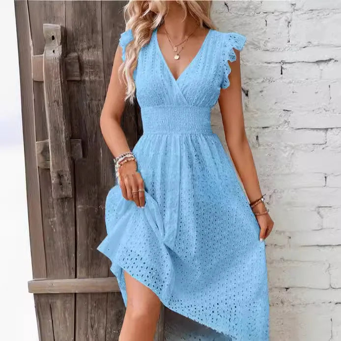 Blue - A woman wearing a white eyelet midi dress with flutter sleeves, a surplice V-neckline, and a wide smocked waistband, standing against a rustic wooden door.
