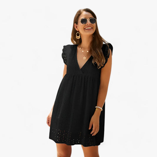 Black - A woman smiling in a black eyelet mini dress with flutter sleeves, a deep V-neckline, and an empire waist, set against a clean white background.