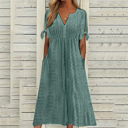 PEACOCK GREEN - A woman wearing a light blue midi-length eyelet dress with a scalloped V-neckline, split tie-sleeves, and side pockets, shown alongside color variations in pink, white, and mint green.