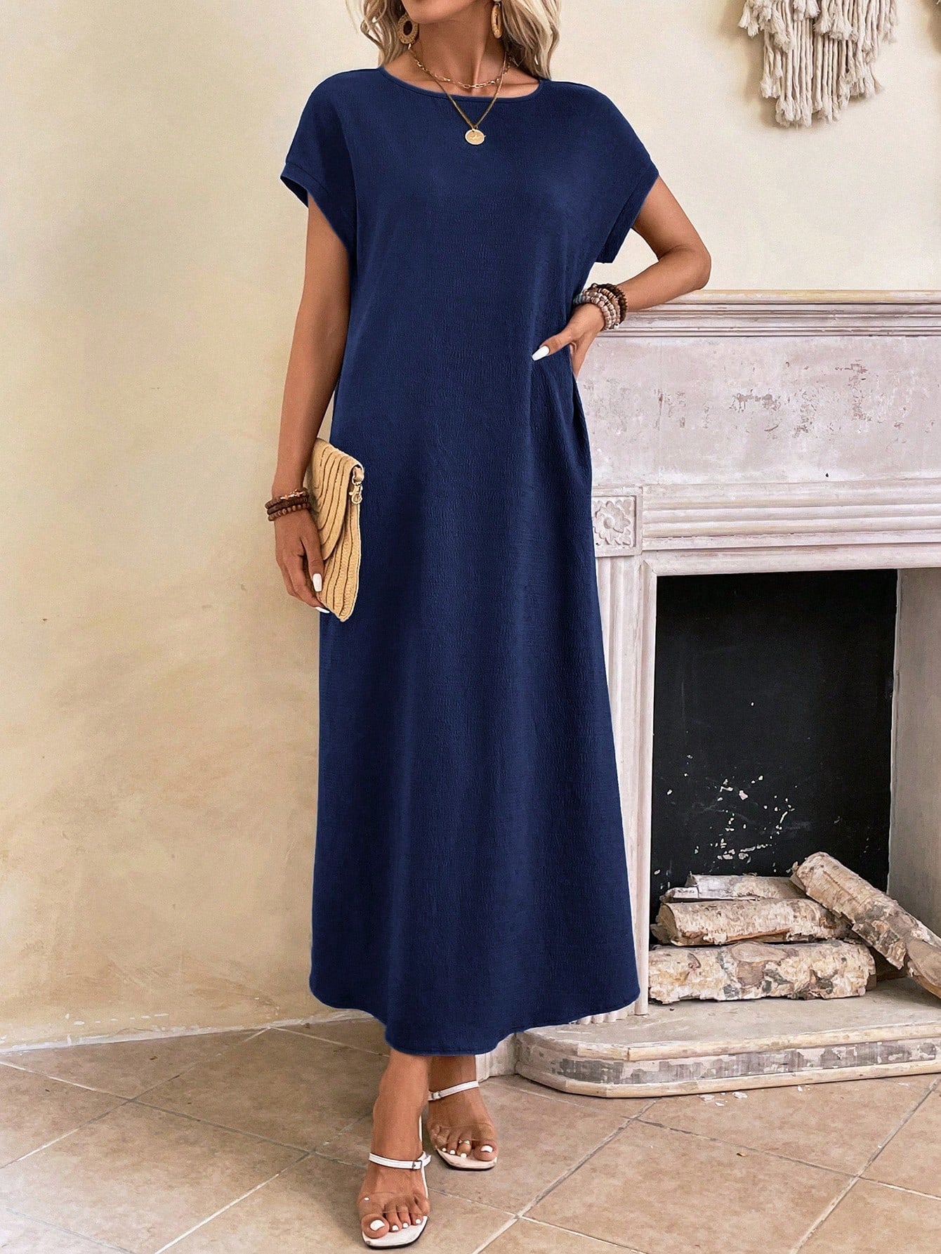Dark Blue - A woman wearing a beige fine-knit maxi dress with cap sleeves and a crew neck, styled with gold jewelry and a woven clutch in a minimalist interior.