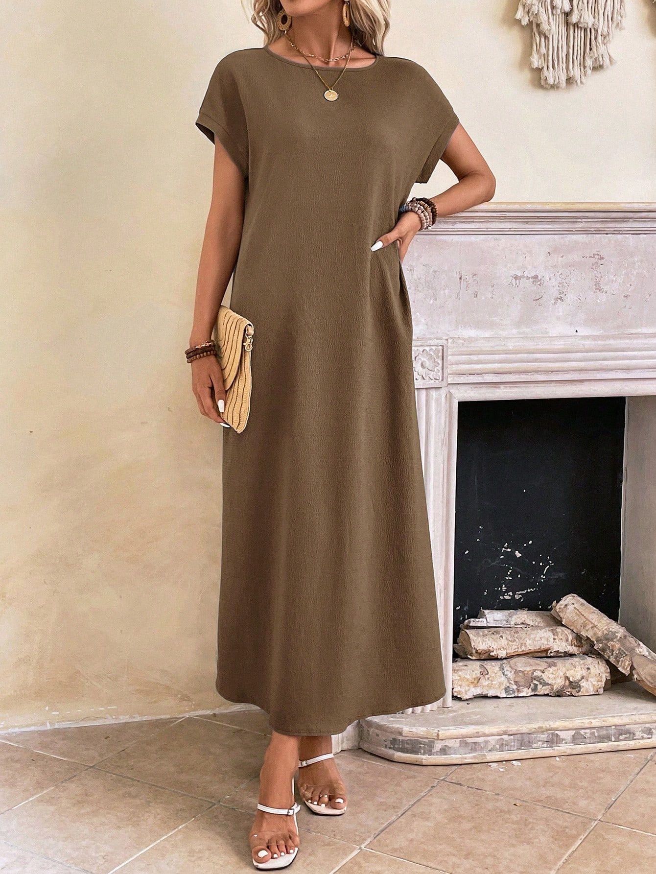 Dark Blue - A woman wearing a beige fine-knit maxi dress with cap sleeves and a crew neck, styled with gold jewelry and a woven clutch in a minimalist interior.