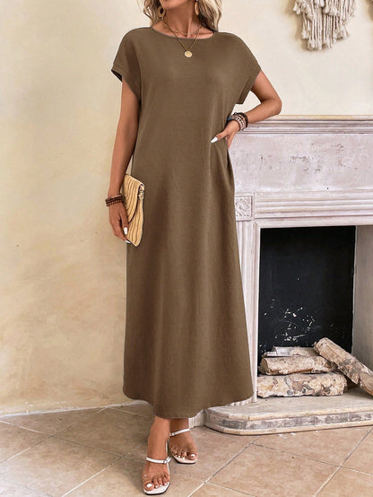 Dark Blue - A woman wearing a beige fine-knit maxi dress with cap sleeves and a crew neck, styled with gold jewelry and a woven clutch in a minimalist interior.