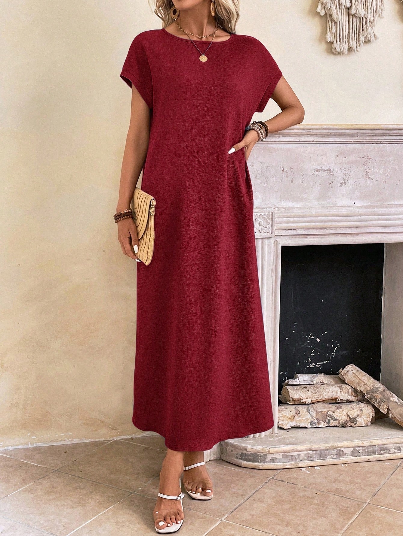 Dark Blue - A woman wearing a beige fine-knit maxi dress with cap sleeves and a crew neck, styled with gold jewelry and a woven clutch in a minimalist interior.