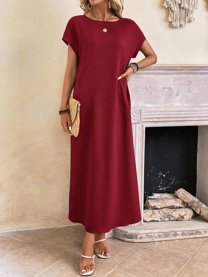 Dark Blue - A woman wearing a beige fine-knit maxi dress with cap sleeves and a crew neck, styled with gold jewelry and a woven clutch in a minimalist interior.