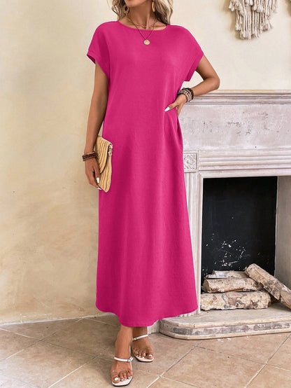 Dark Blue - A woman wearing a beige fine-knit maxi dress with cap sleeves and a crew neck, styled with gold jewelry and a woven clutch in a minimalist interior.