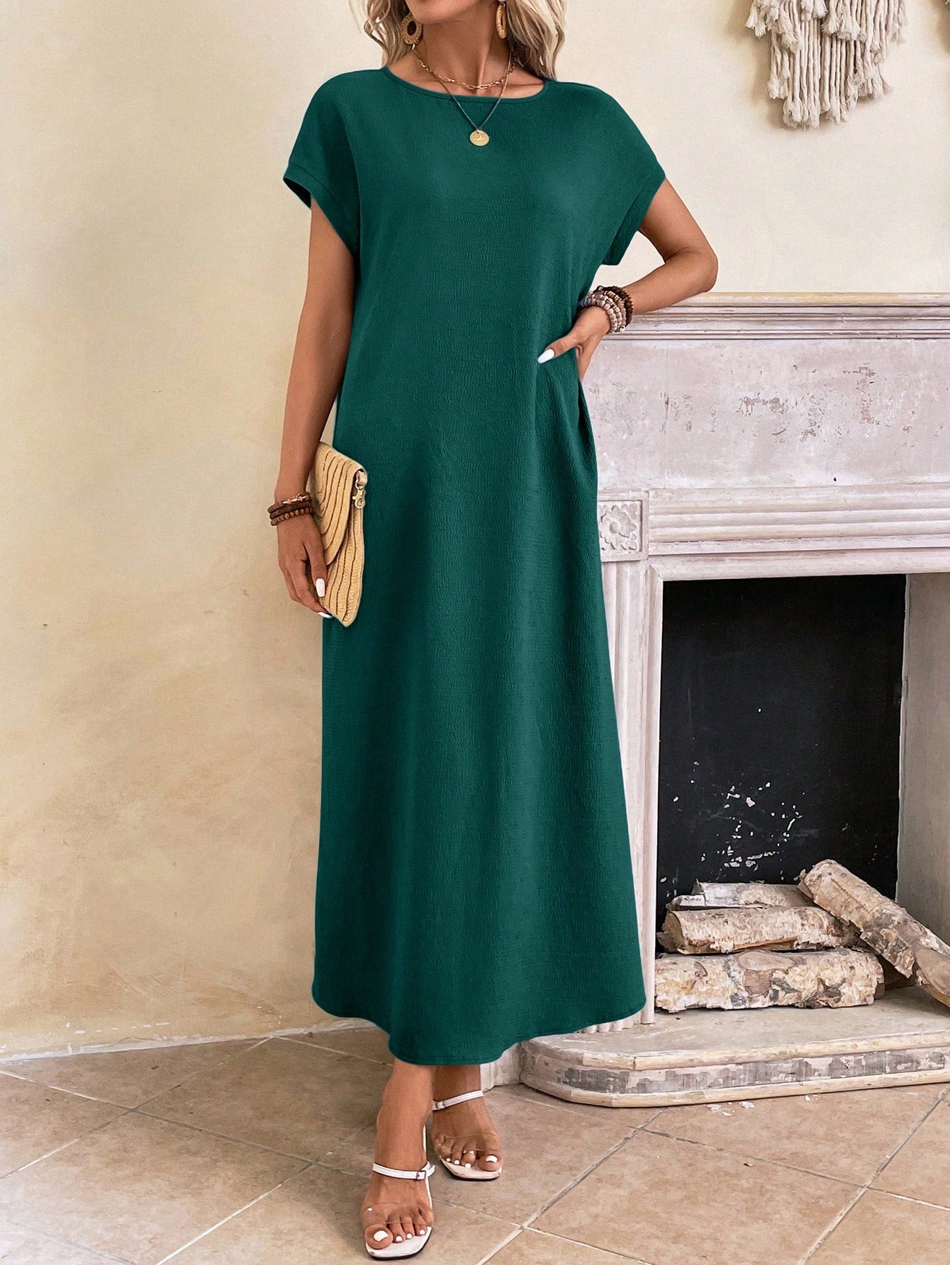 Dark Blue - A woman wearing a beige fine-knit maxi dress with cap sleeves and a crew neck, styled with gold jewelry and a woven clutch in a minimalist interior.
