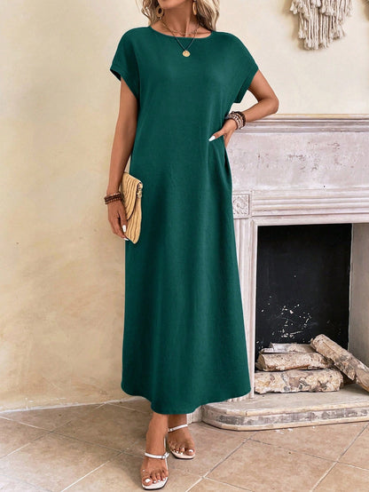 Dark Blue - A woman wearing a beige fine-knit maxi dress with cap sleeves and a crew neck, styled with gold jewelry and a woven clutch in a minimalist interior.
