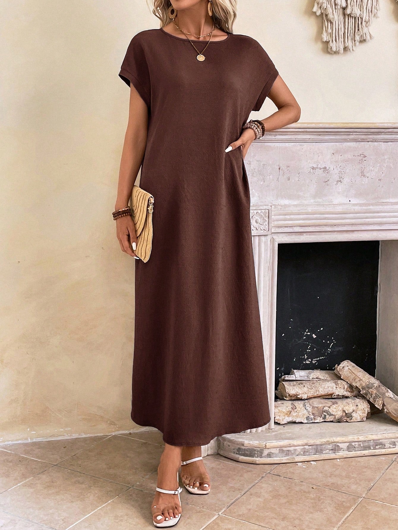 Dark Blue - A woman wearing a beige fine-knit maxi dress with cap sleeves and a crew neck, styled with gold jewelry and a woven clutch in a minimalist interior.