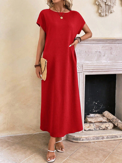 Dark Blue - A woman wearing a beige fine-knit maxi dress with cap sleeves and a crew neck, styled with gold jewelry and a woven clutch in a minimalist interior.