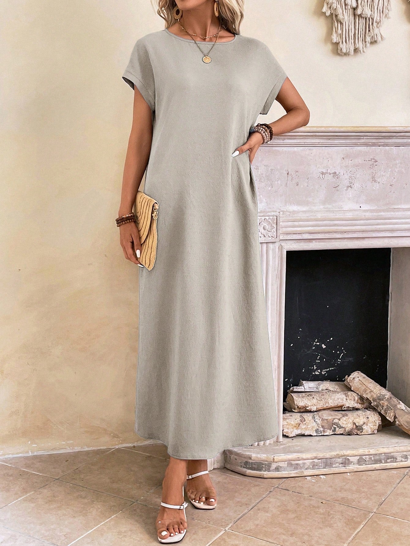 Dark Blue - A woman wearing a beige fine-knit maxi dress with cap sleeves and a crew neck, styled with gold jewelry and a woven clutch in a minimalist interior.