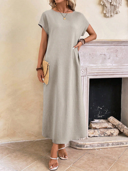 Dark Blue - A woman wearing a beige fine-knit maxi dress with cap sleeves and a crew neck, styled with gold jewelry and a woven clutch in a minimalist interior.