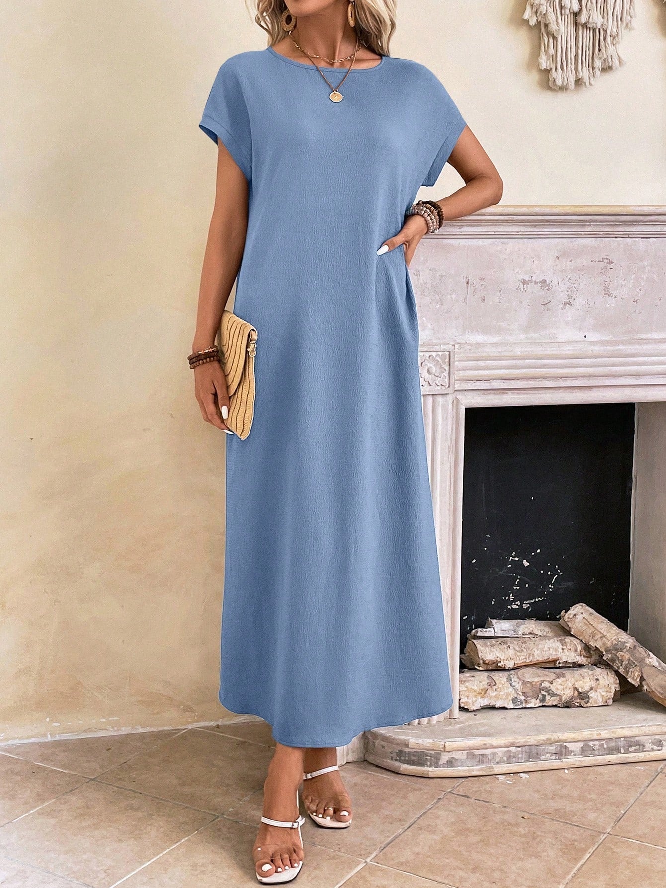 Dark Blue - A woman wearing a beige fine-knit maxi dress with cap sleeves and a crew neck, styled with gold jewelry and a woven clutch in a minimalist interior.