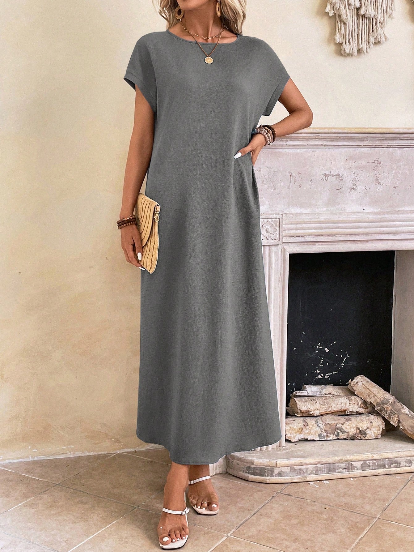 Dark Blue - A woman wearing a beige fine-knit maxi dress with cap sleeves and a crew neck, styled with gold jewelry and a woven clutch in a minimalist interior.