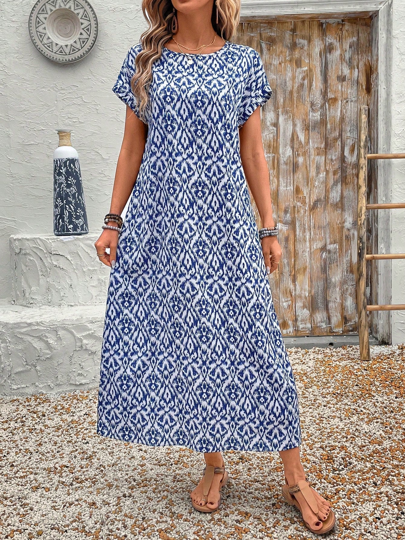 Dark Blue - A woman wearing a beige fine-knit maxi dress with cap sleeves and a crew neck, styled with gold jewelry and a woven clutch in a minimalist interior.