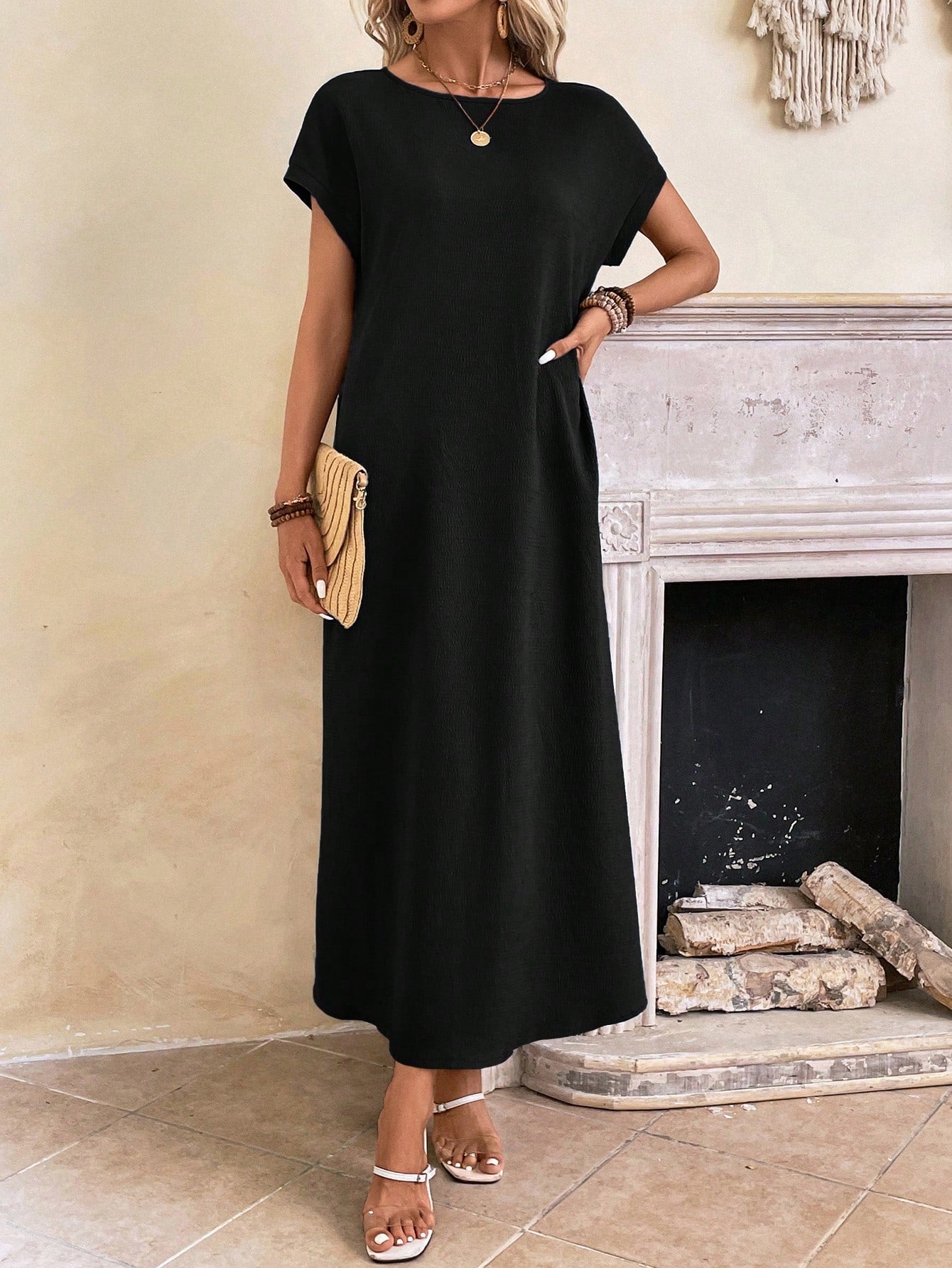 Obscure Blue - A woman wearing a beige fine-knit maxi dress with cap sleeves and a crew neck, styled with gold jewelry and a woven clutch in a minimalist interior.