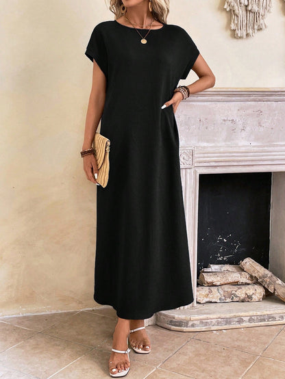 Obscure Blue - A woman wearing a beige fine-knit maxi dress with cap sleeves and a crew neck, styled with gold jewelry and a woven clutch in a minimalist interior.