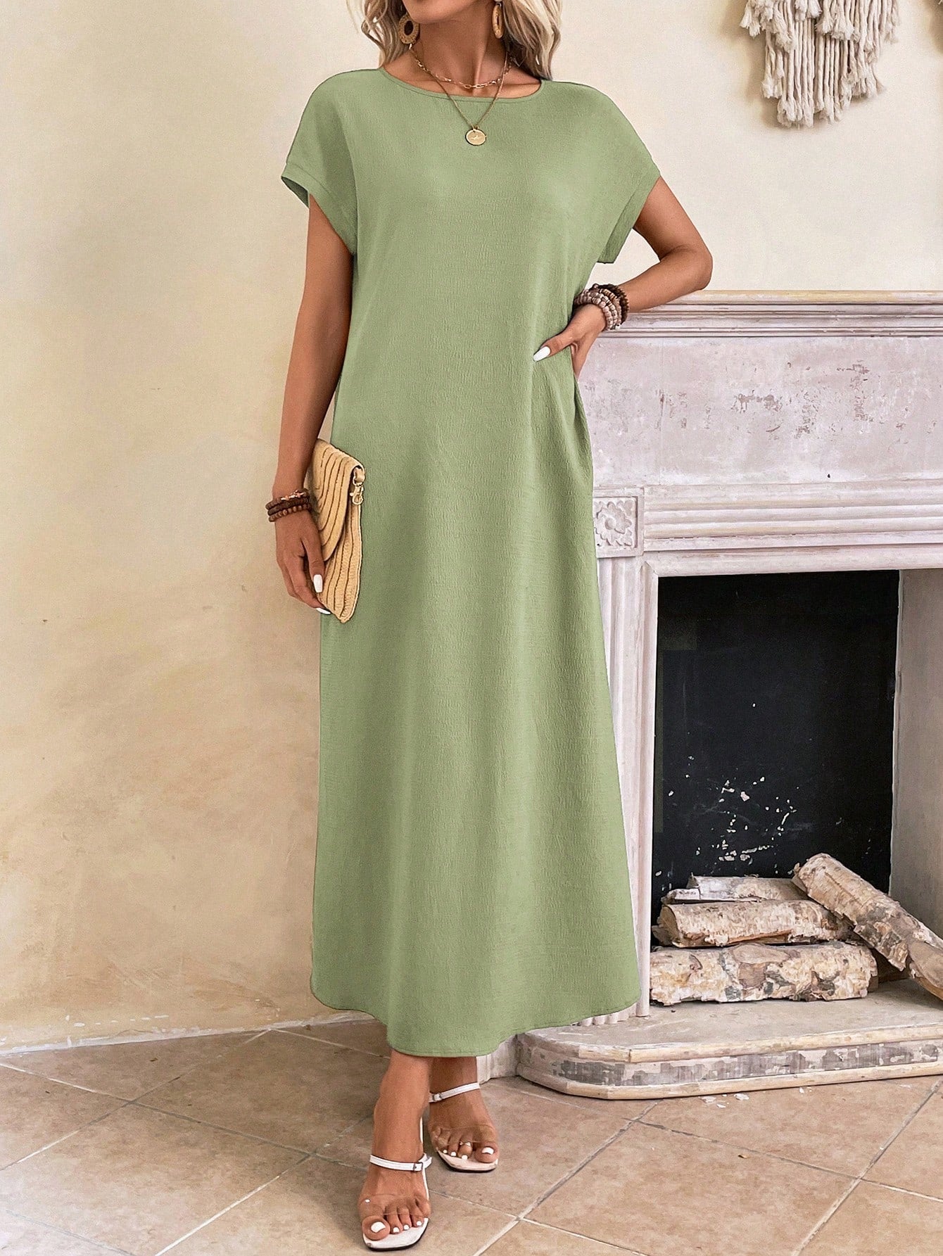 Obscure Blue - A woman wearing a beige fine-knit maxi dress with cap sleeves and a crew neck, styled with gold jewelry and a woven clutch in a minimalist interior.