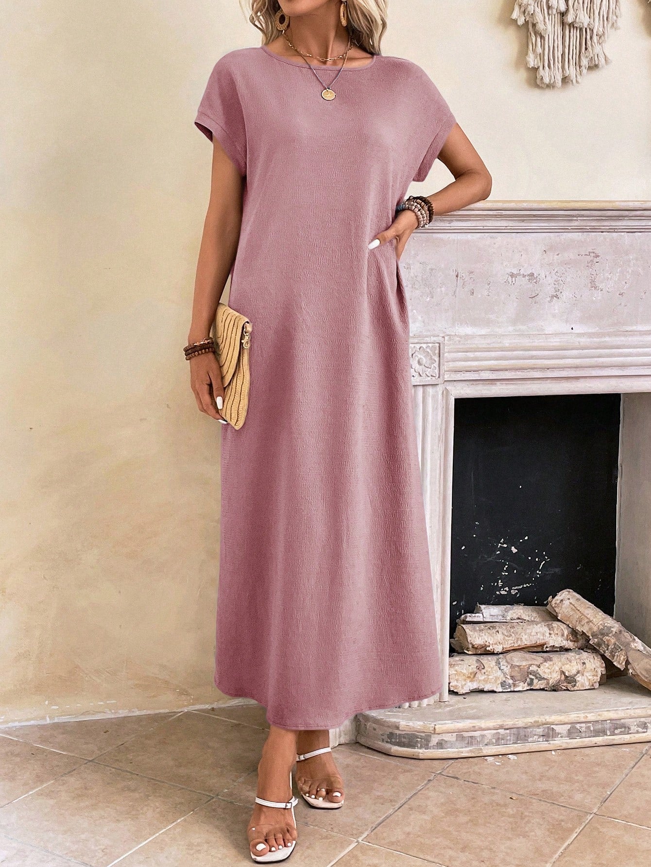 Obscure Blue - A woman wearing a beige fine-knit maxi dress with cap sleeves and a crew neck, styled with gold jewelry and a woven clutch in a minimalist interior.