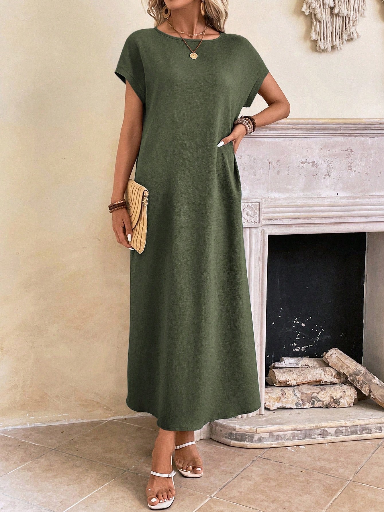 Obscure Blue - A woman wearing a beige fine-knit maxi dress with cap sleeves and a crew neck, styled with gold jewelry and a woven clutch in a minimalist interior.
