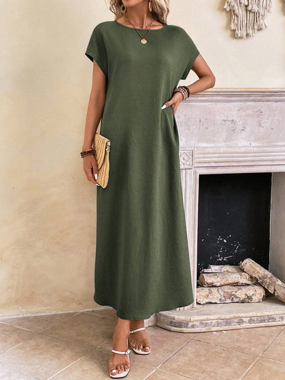 Obscure Blue - A woman wearing a beige fine-knit maxi dress with cap sleeves and a crew neck, styled with gold jewelry and a woven clutch in a minimalist interior.