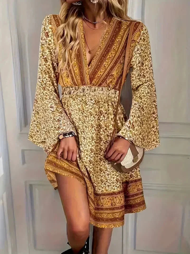 Mixed floral print mini dress in earthy mustard and brown tones featuring a deep V-neckline, wide smocked waist, and long bell sleeves.