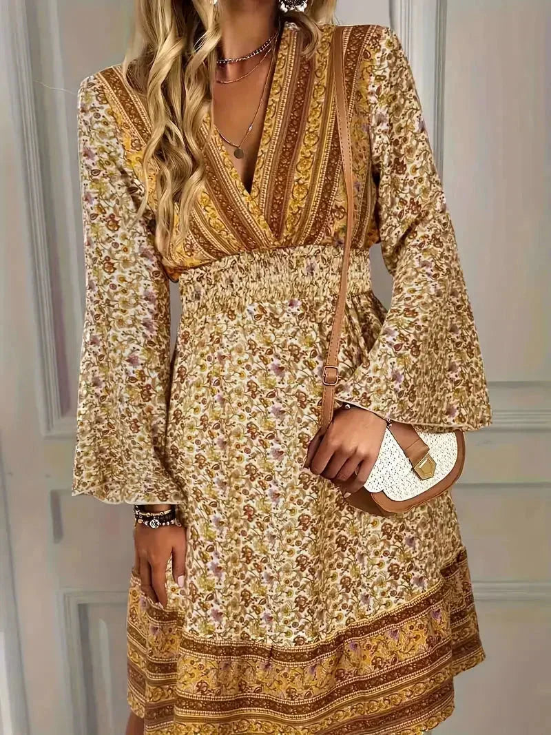 Mixed floral print mini dress in earthy mustard and brown tones featuring a deep V-neckline, wide smocked waist, and long bell sleeves.