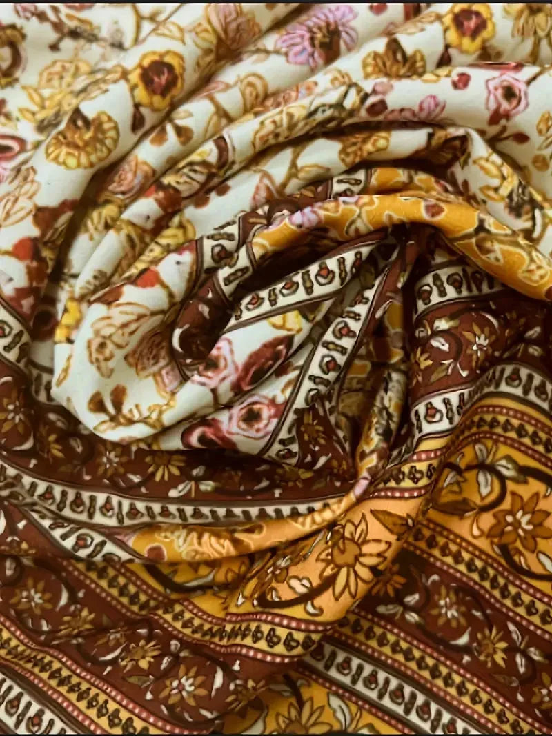 Mixed floral print mini dress in earthy mustard and brown tones featuring a deep V-neckline, wide smocked waist, and long bell sleeves.