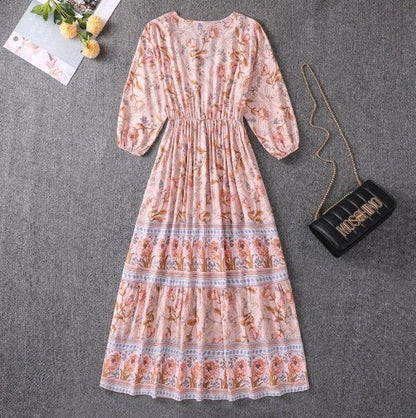 Orange - A woman wearing a light blue midi dress with a botanical floral border print, featuring a V-neckline, three-quarter sleeves, and a tiered skirt.